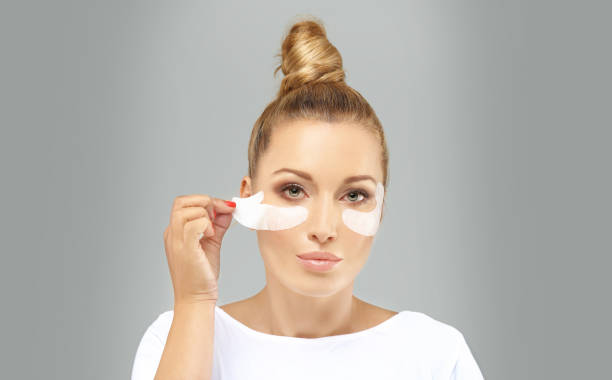 A woman applies under-eye patches to reduce bags and circles as part of a beauty routine.