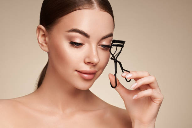 Woman demonstrating proper use of an eyelash curler by carefully aligning it with her lashes.