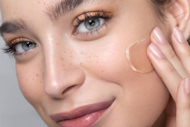 Close-up of a woman applying foundation to her cheek, highlighting smooth and healthy skin.